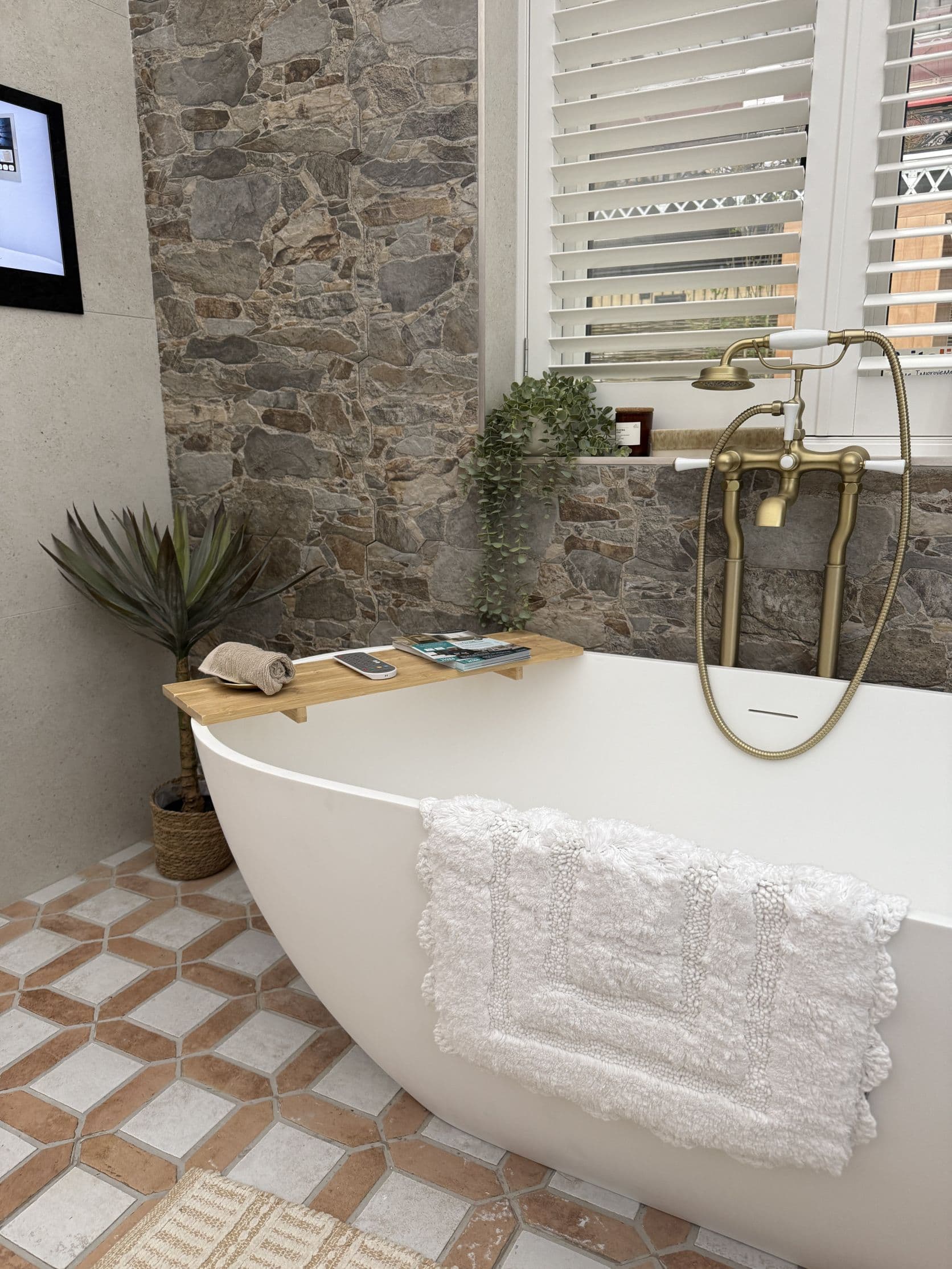 Freestanding bath with brushed brass taps, patterned wall tiles and detailed floor tiling by FP Bathrooms